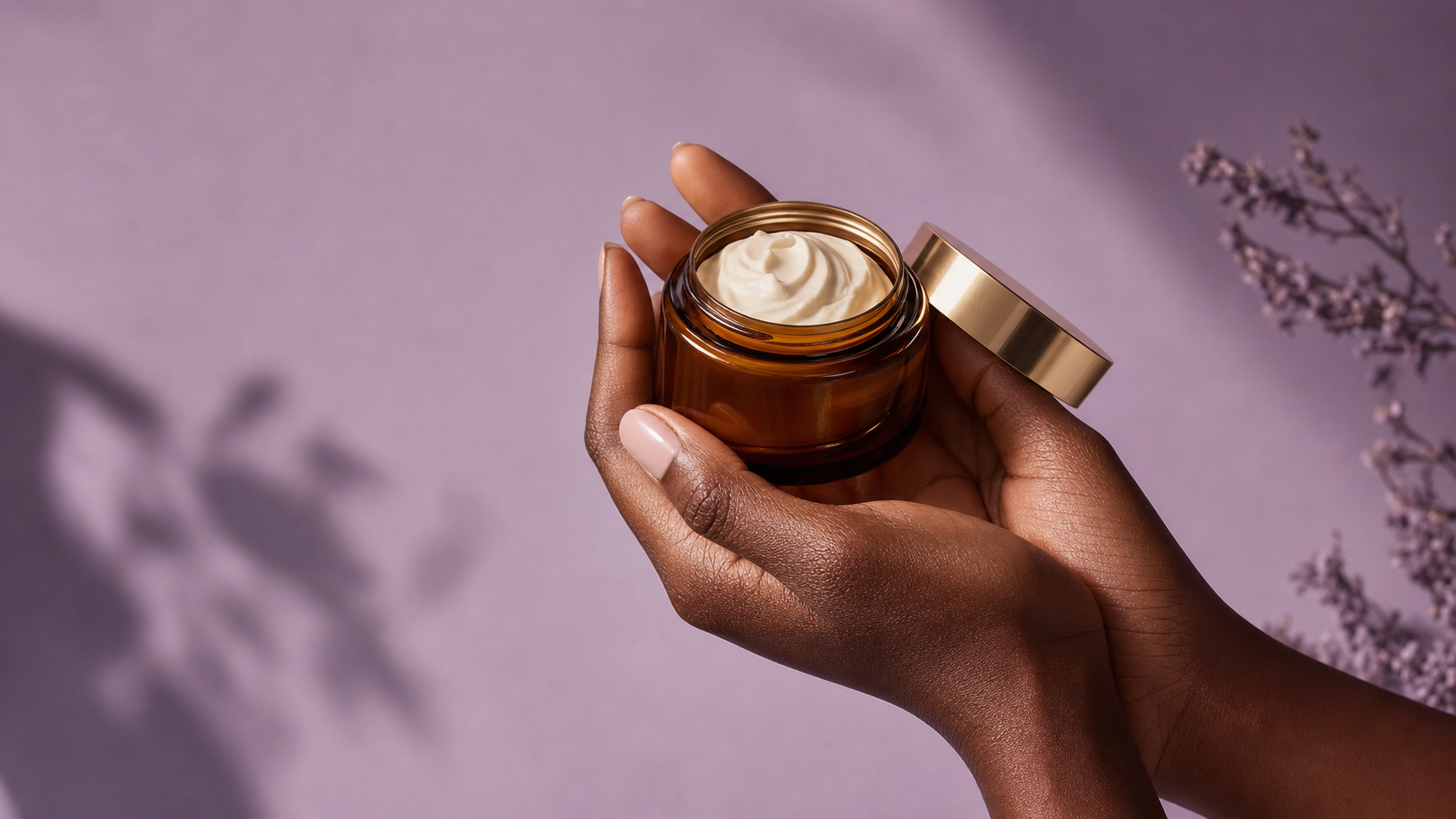 Hands holding a small jar of whipped body butter on a soft lavender background